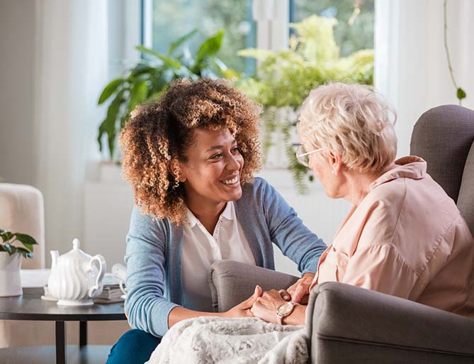 A nurse warmly interacting with an elderly woman in a cozy, well-lit living unit.