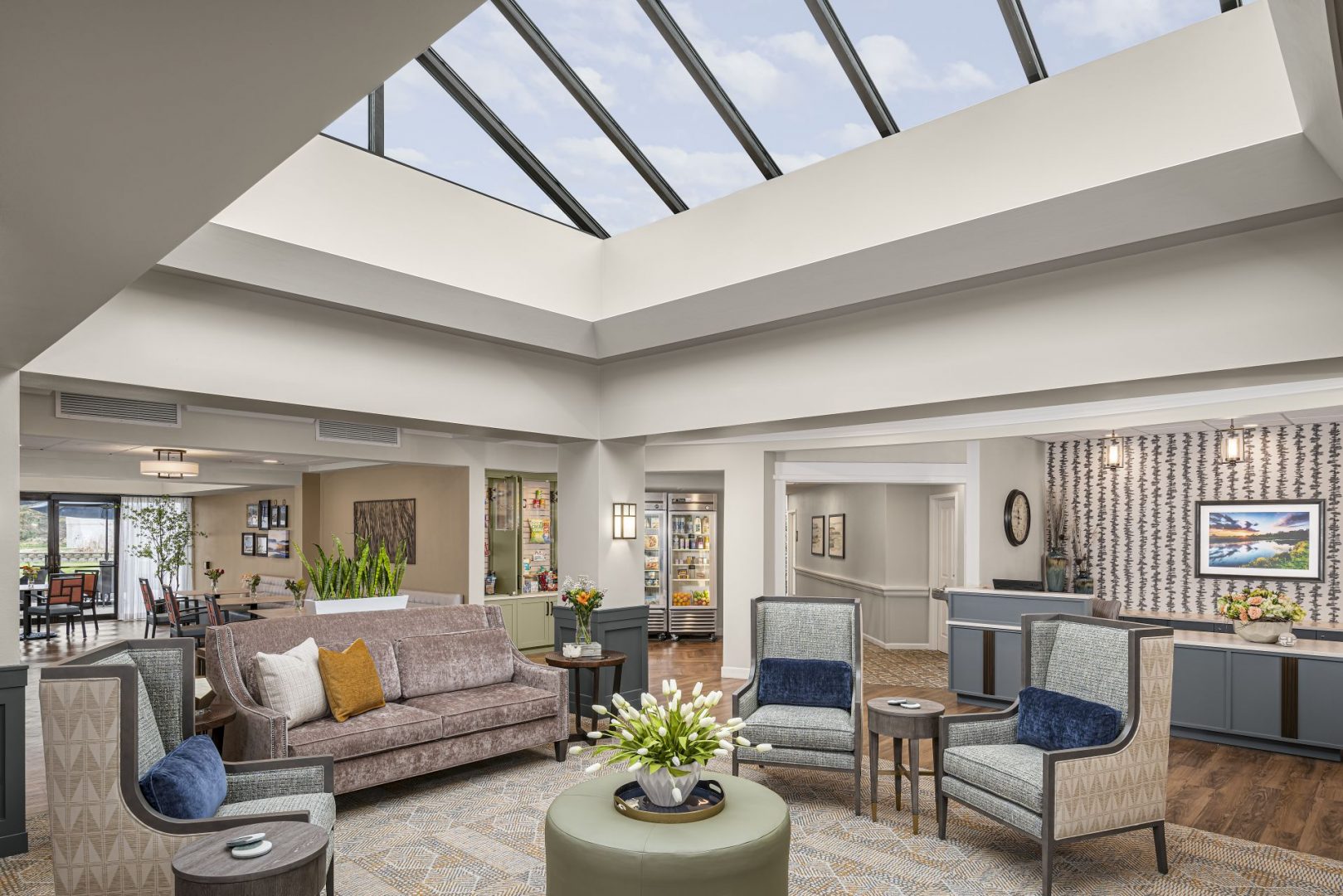 Bright and spacious lobby area with chairs, a sofa, skylight, and decorative plants.