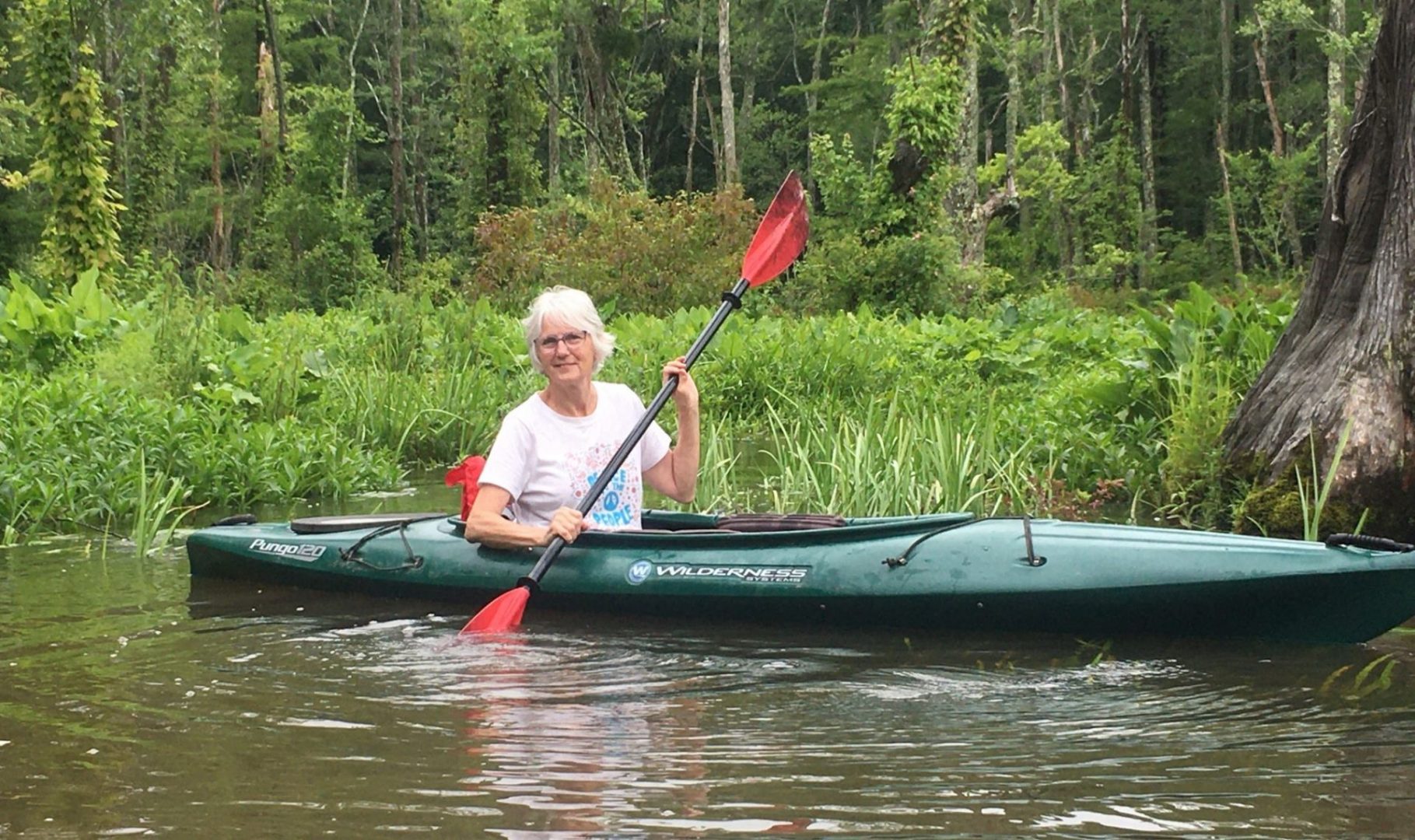 Woman kayaking on a serene lake surrounded by lush green trees and vegetation.