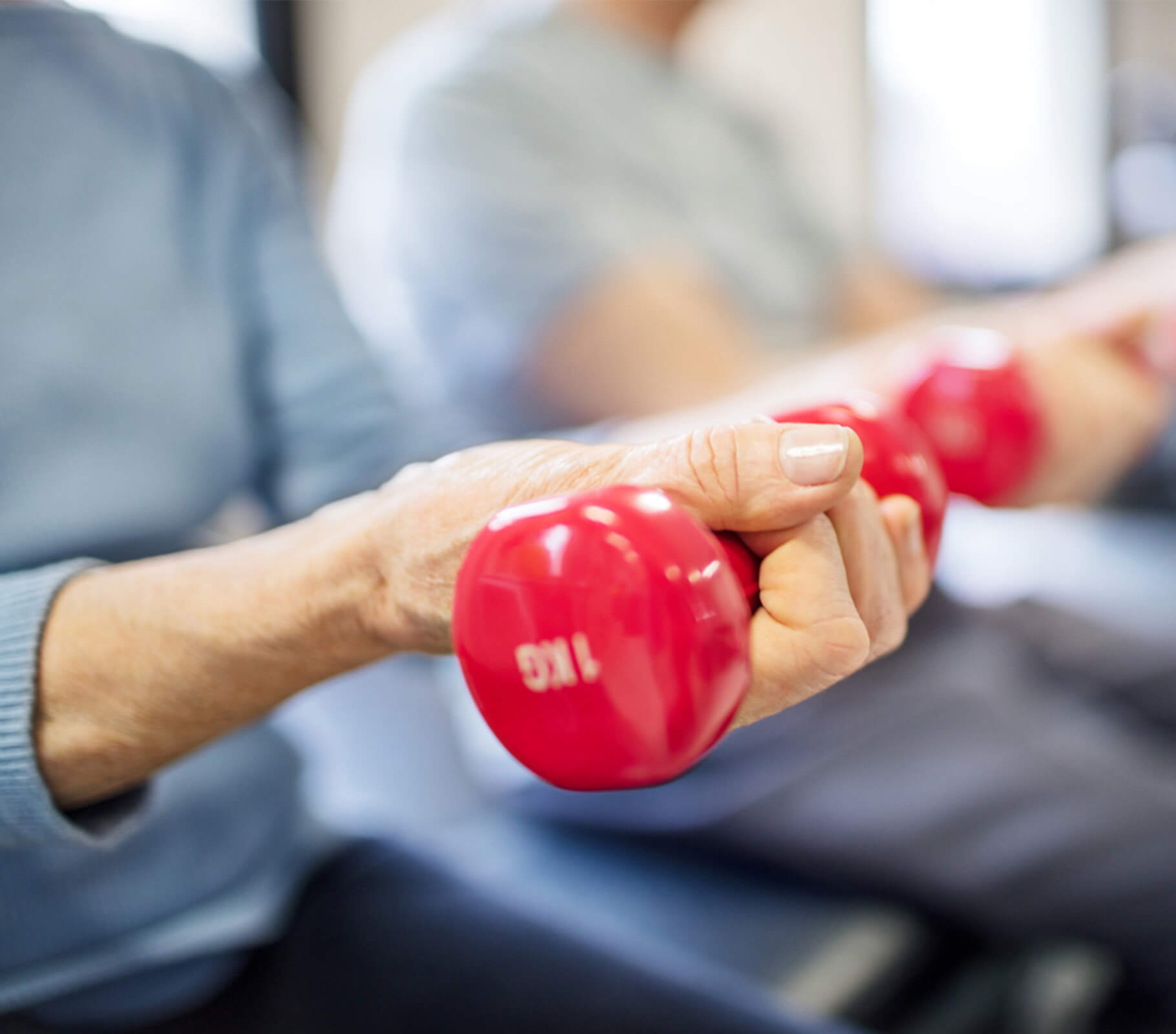 Senior individual exercising with red dumbbells in a group setting.