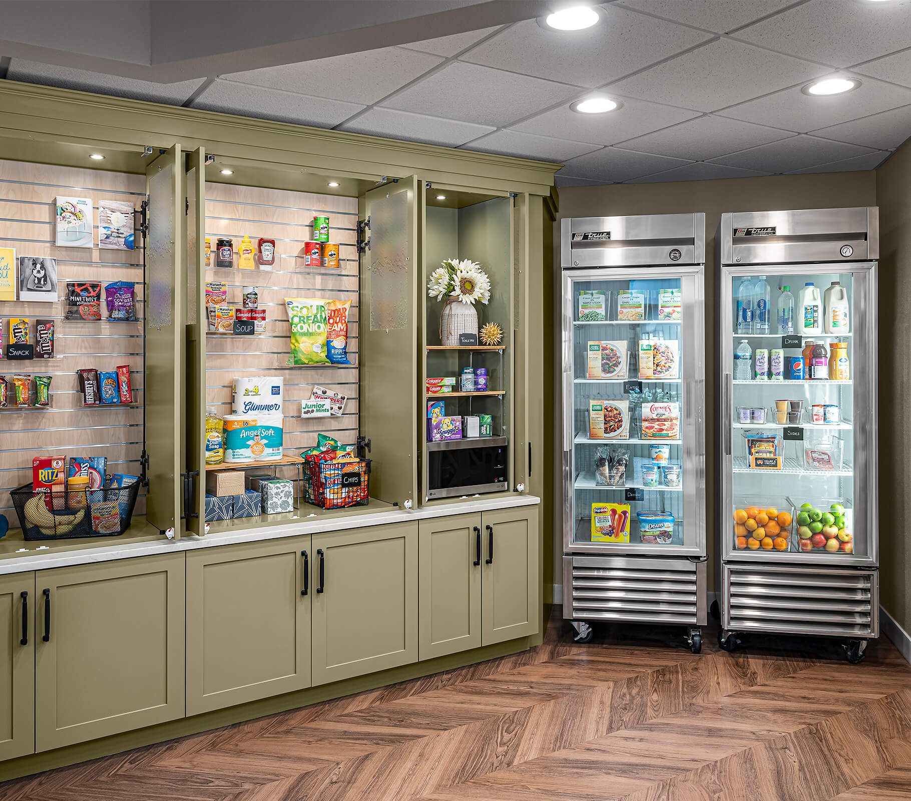 Pantry area with food and drinks in a community unit, featuring shelves and refrigerators.