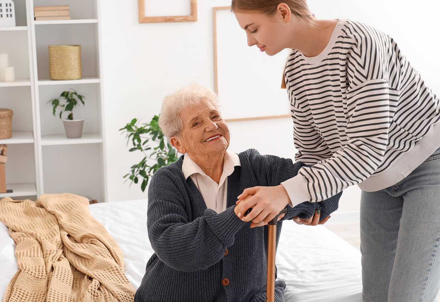Caregiver assisting a senior woman with a cane in a cozy living space.