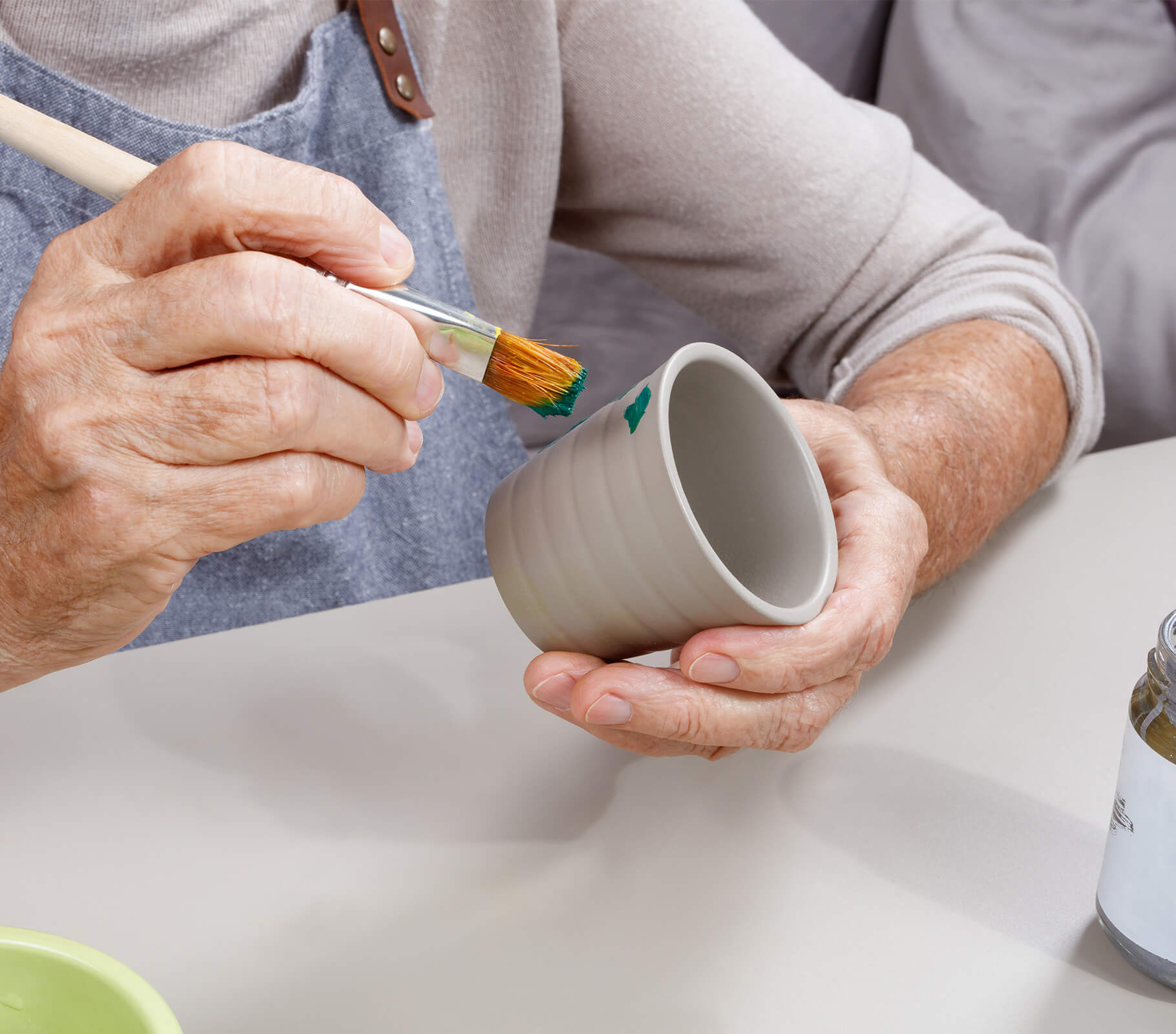 Senior individual painting a small ceramic cup with a brush.