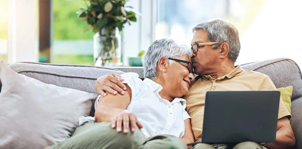 Elderly couple cuddling on a couch with a laptop in a cozy unit setting.