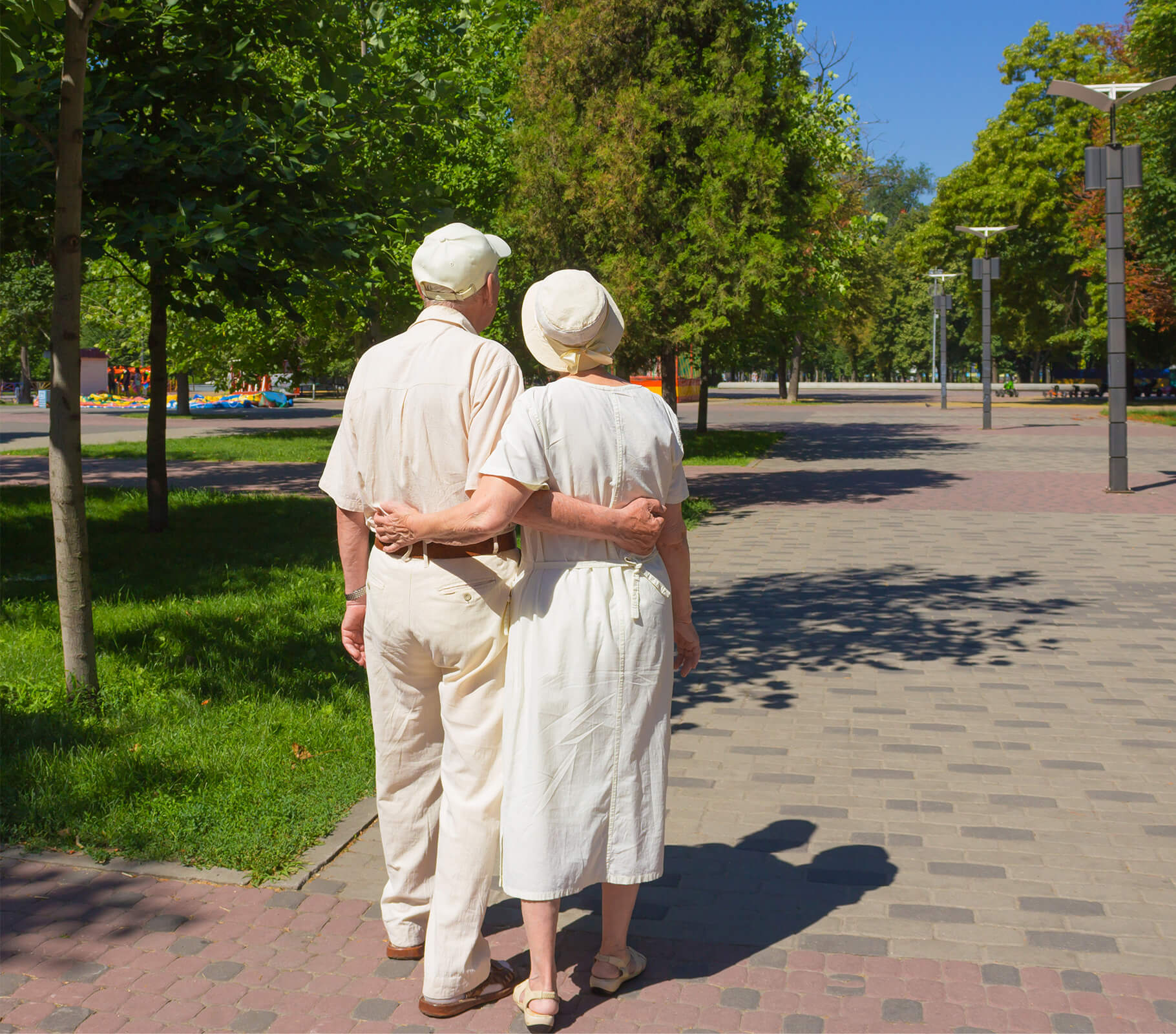 Elderly couple walking in a park on a sunny day, surrounded by trees.