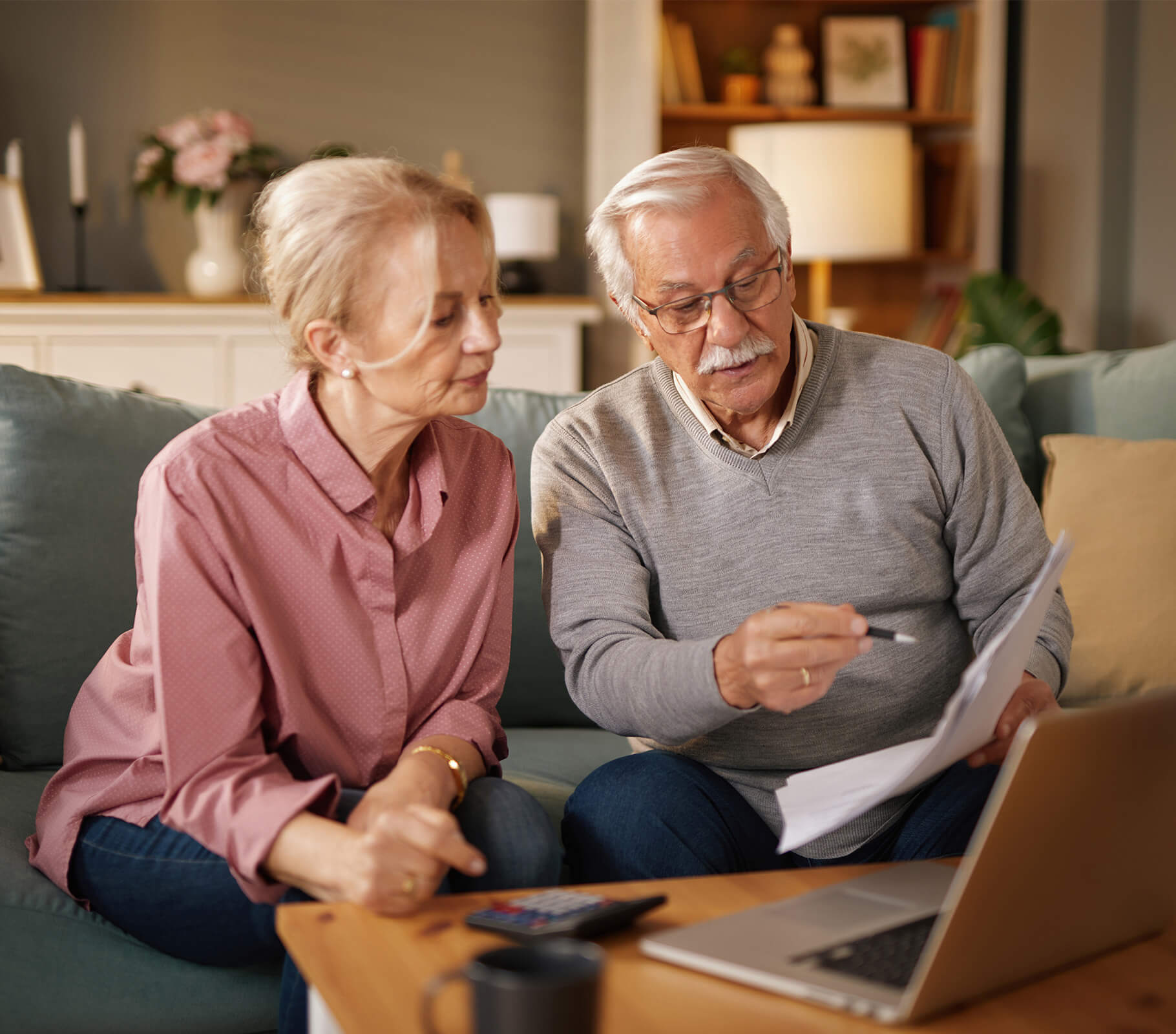 Elderly couple reviewing documents together in their living room with a laptop.