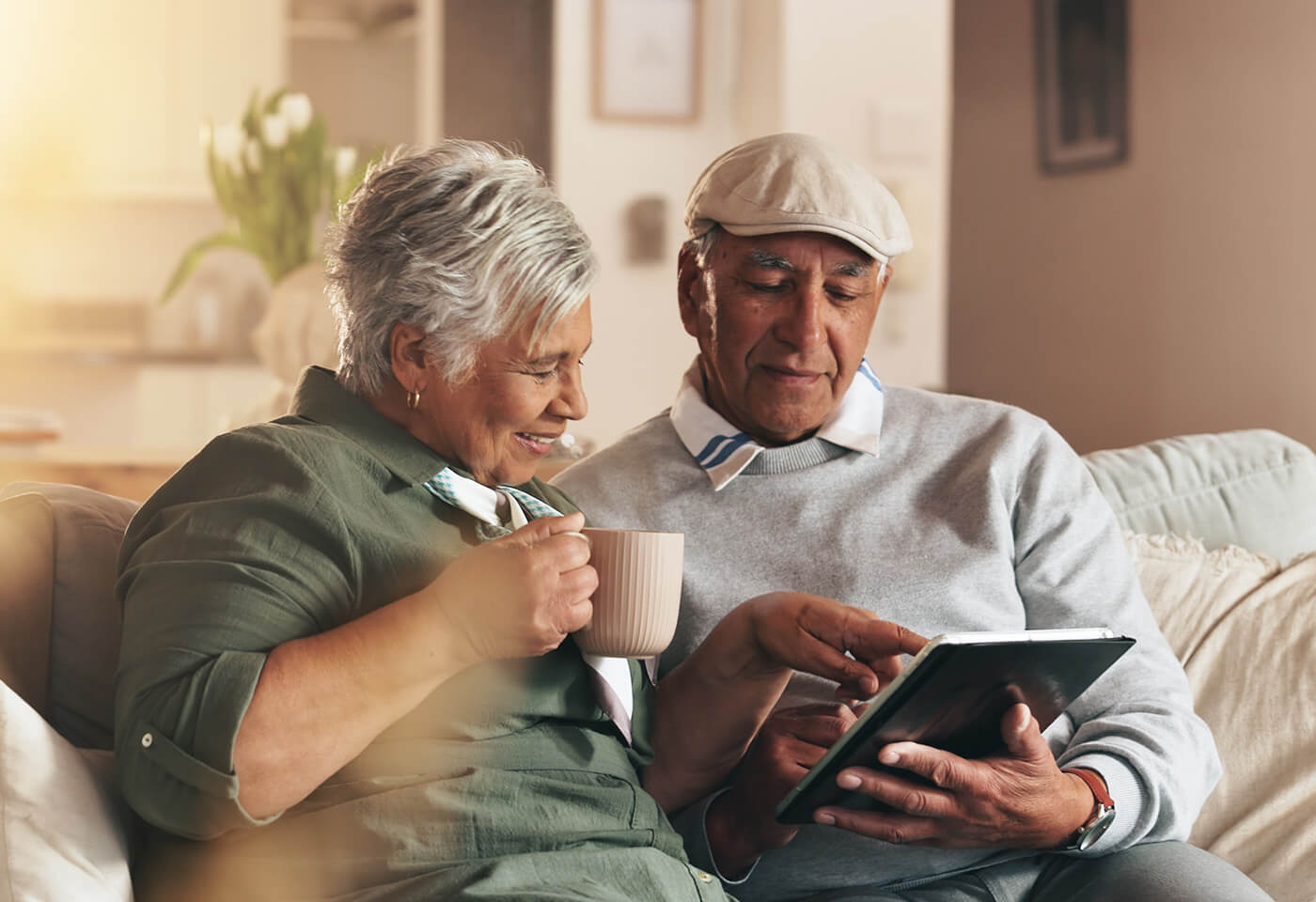 Smiling elderly couple using a tablet together on a cozy sofa in their living space.