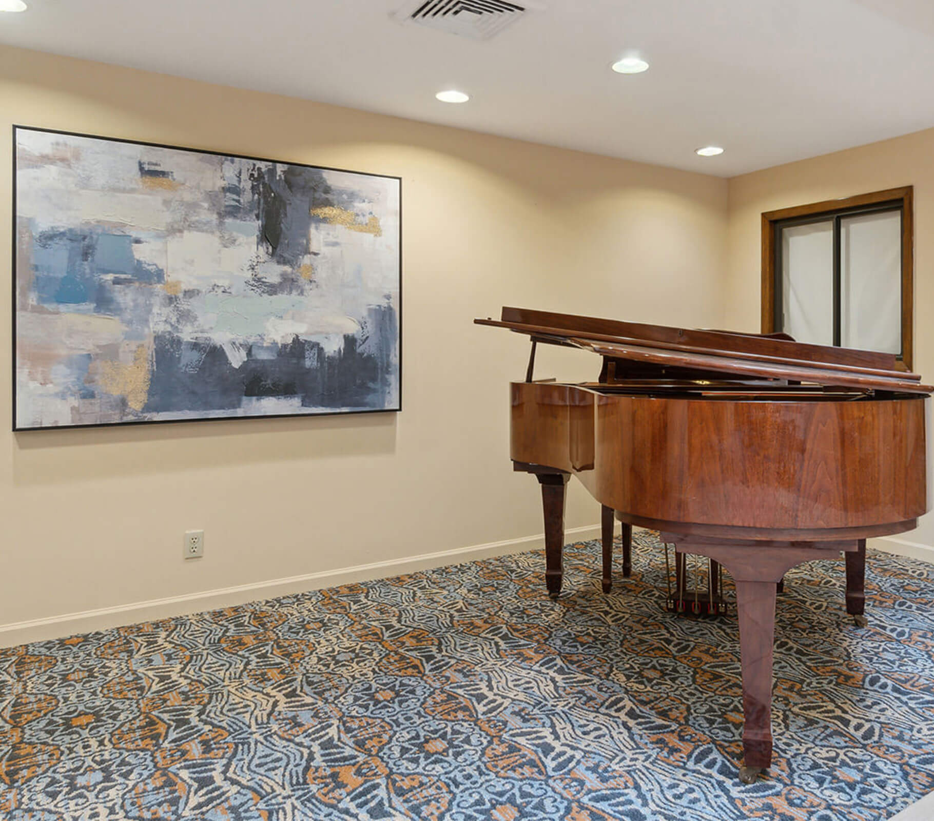 Grand piano and abstract painting in a warmly lit room with patterned carpet.