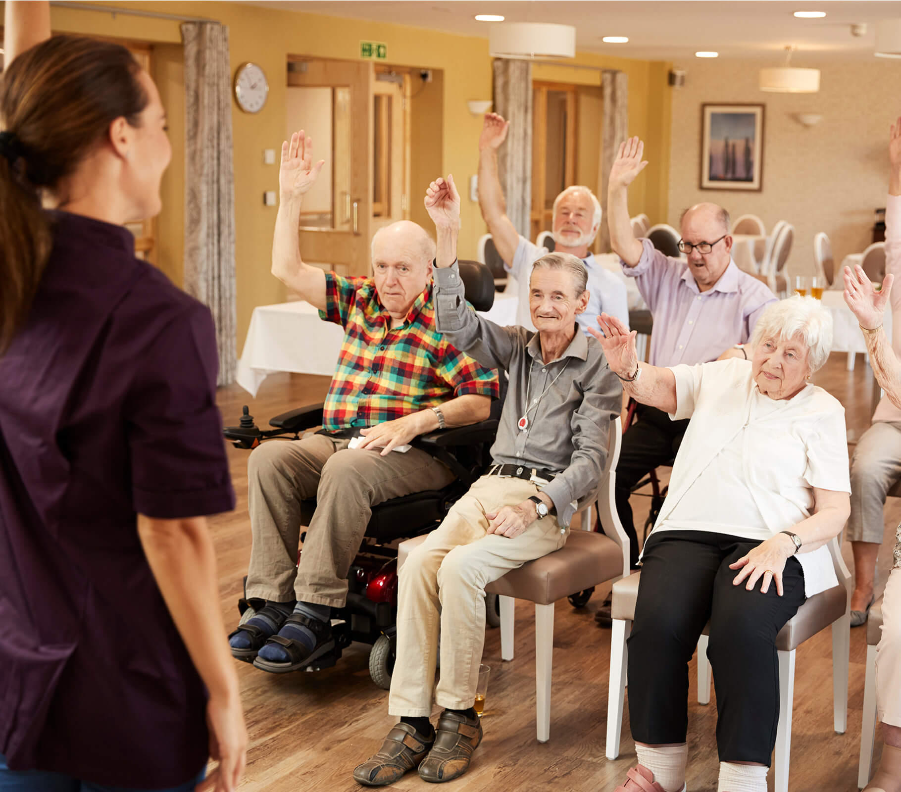 Residents in group activity at a senior community, raising hands enthusiastically.