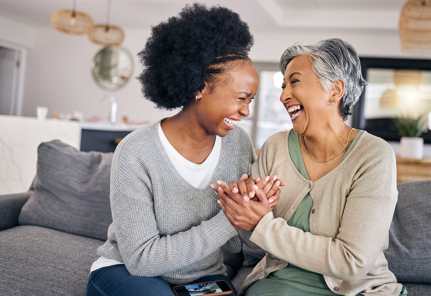 Two women sharing a joyful moment on a couch in a bright living space.