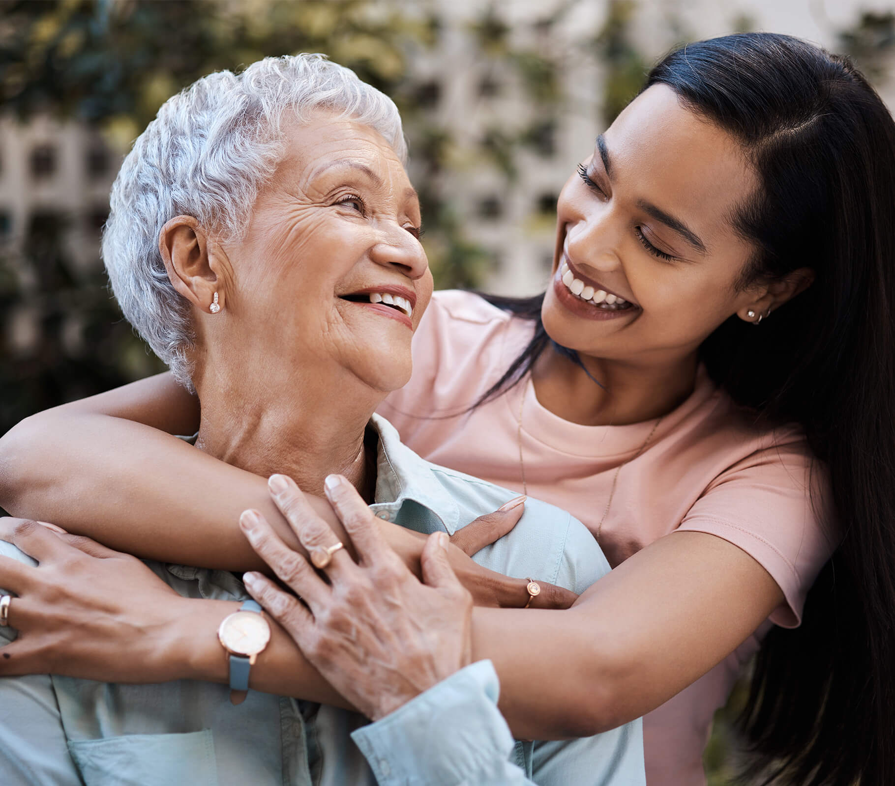 Two women smiling during a warm embrace in an outdoor setting.