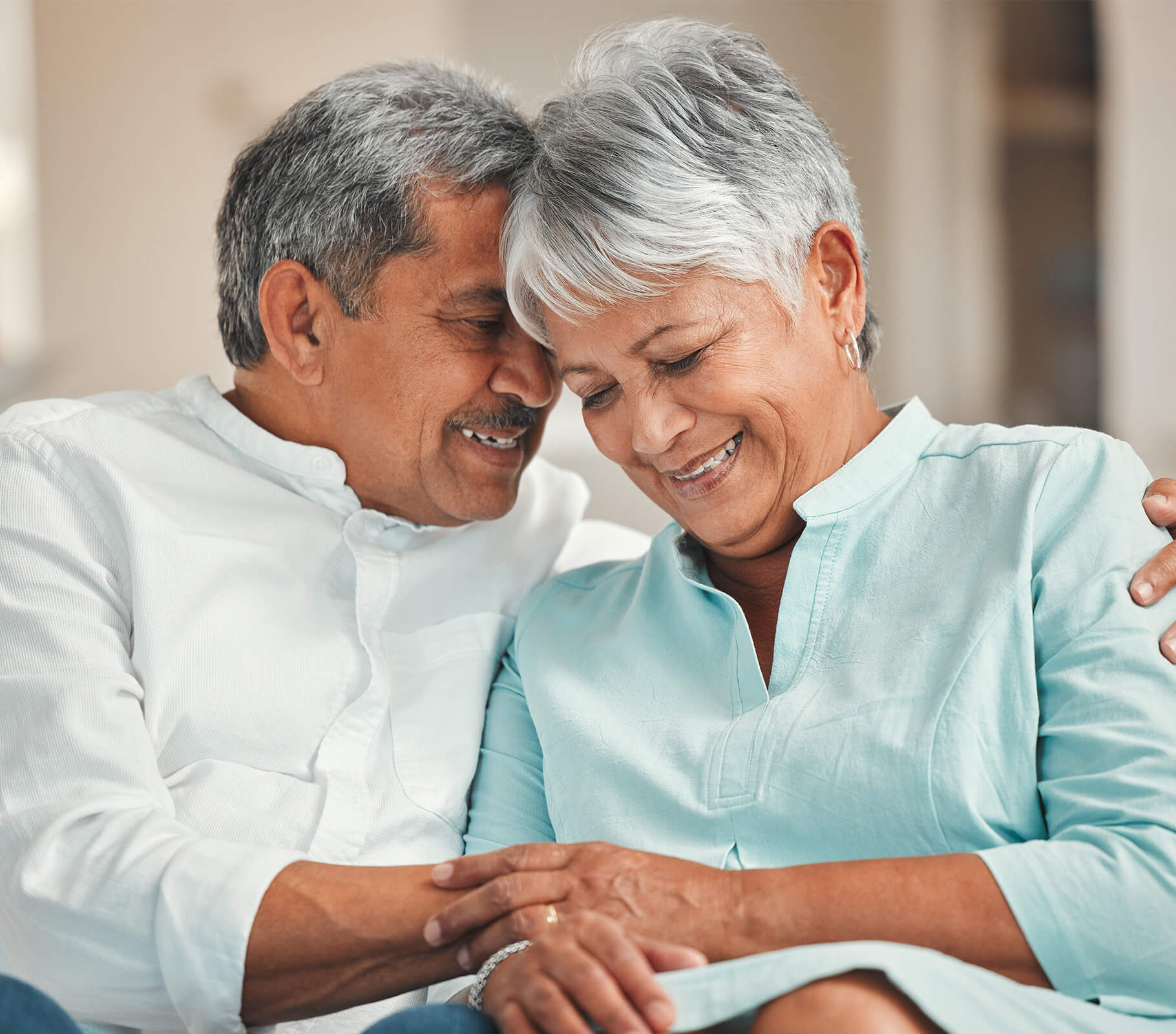 Happy elderly couple sitting closely, smiling together inside a cozy room.