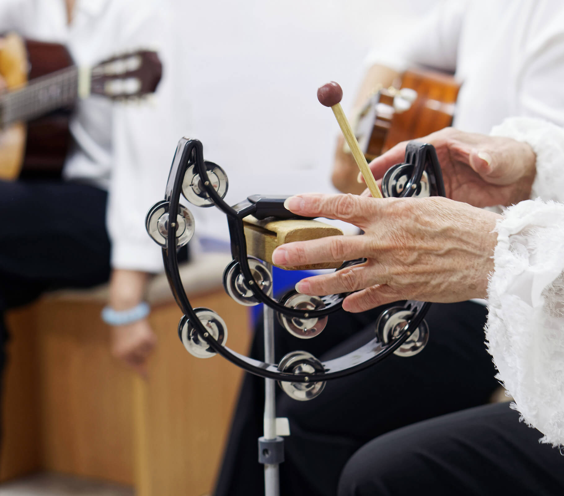 Senior playing tambourine with musicians, engaged in a group activity.