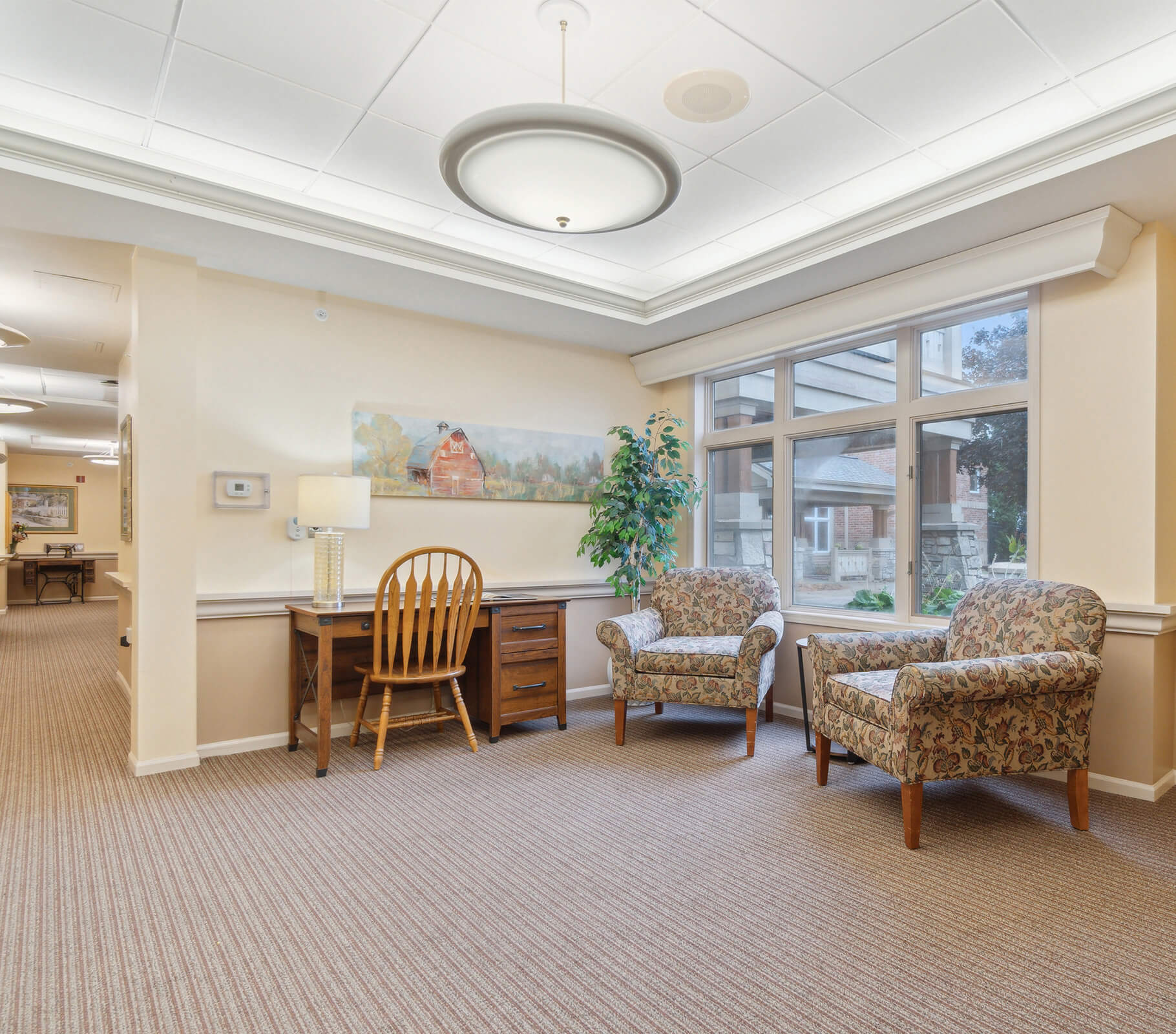 Bright living area with chairs, desk, and large window in senior living community.