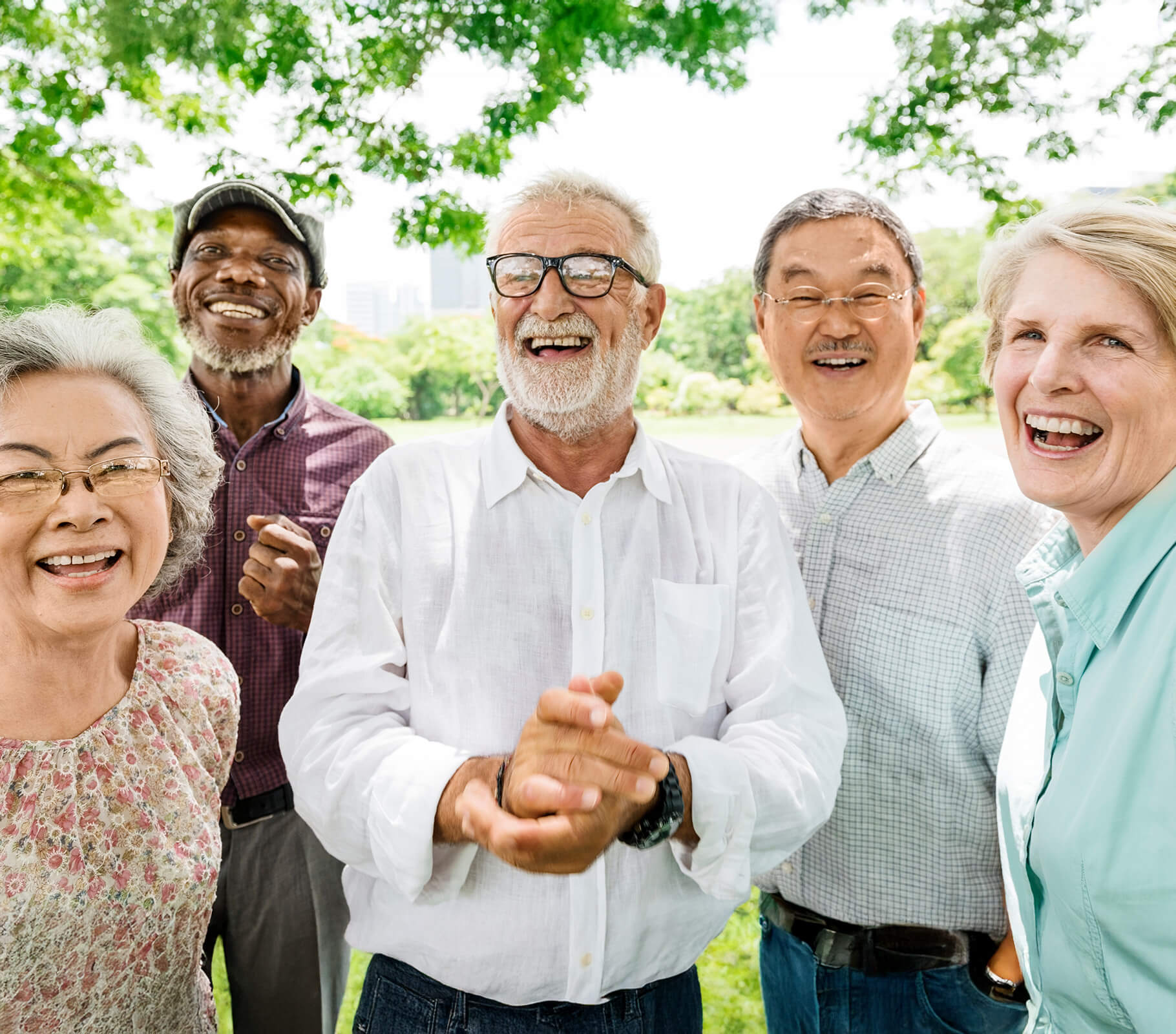 Diverse group of seniors smiling outdoors under lush green trees.