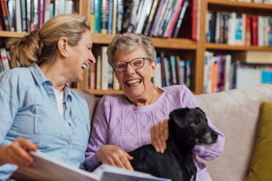 Senior woman laughing with daughter on the couch while they sit with a dog