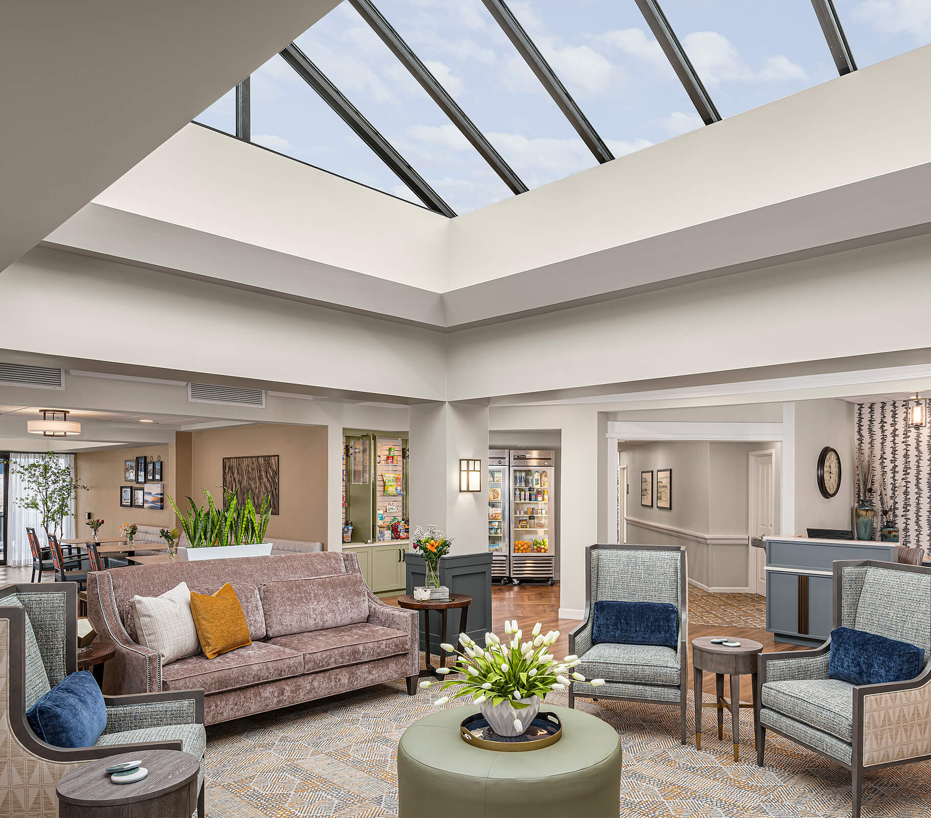 Spacious lounge with skylight, sofas, chairs, and plants in a senior living community.