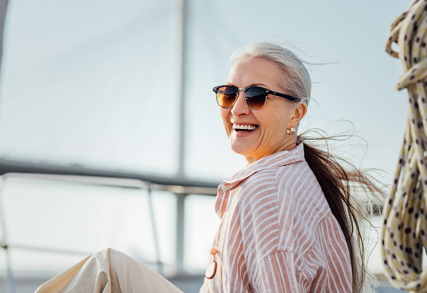Smiling woman with sunglasses enjoying a sunny day outdoors on a boat.