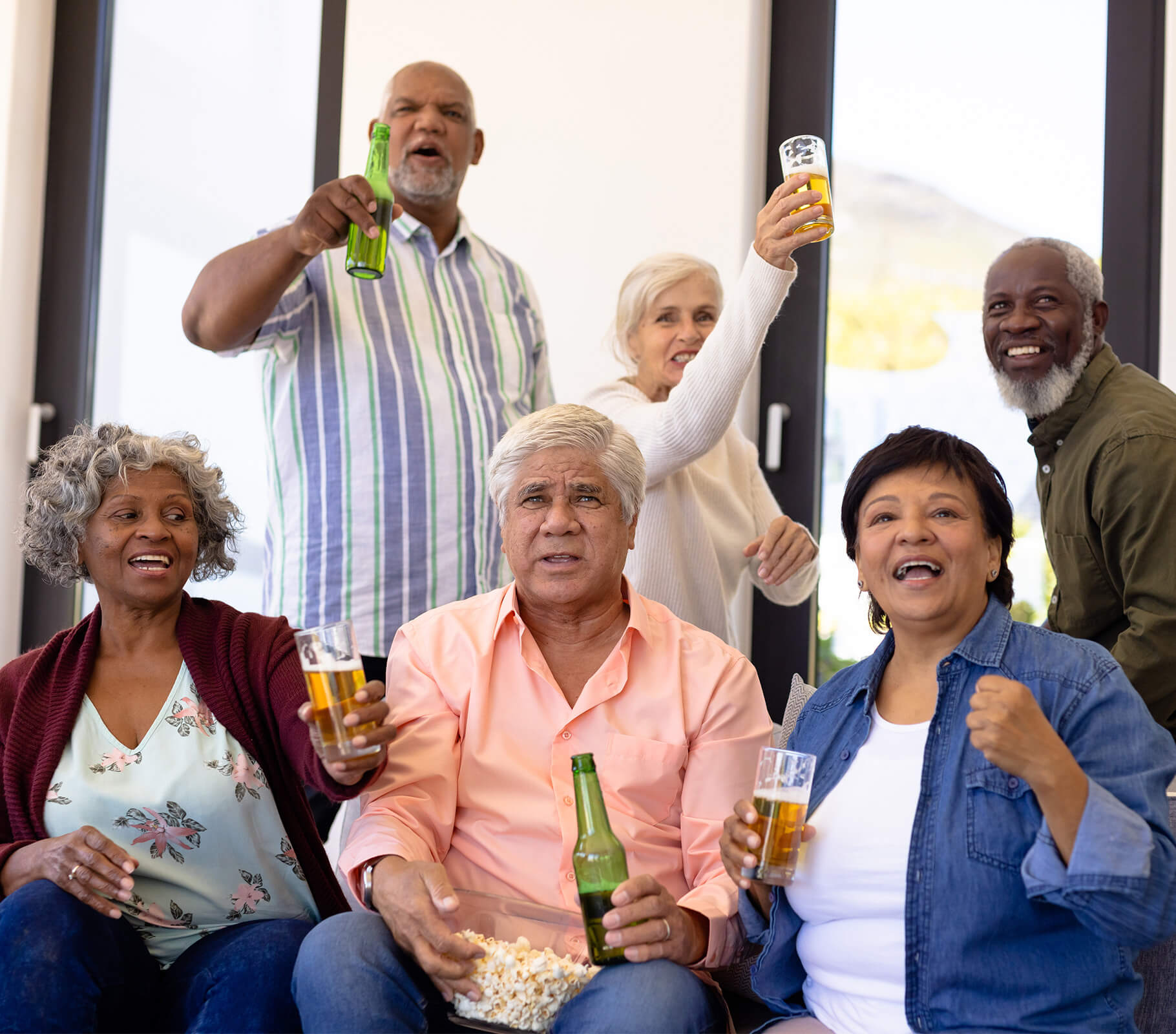 Group of six seniors enjoying drinks and socializing in a bright room.