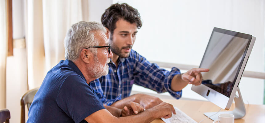 Adult son helping his dad use a computer