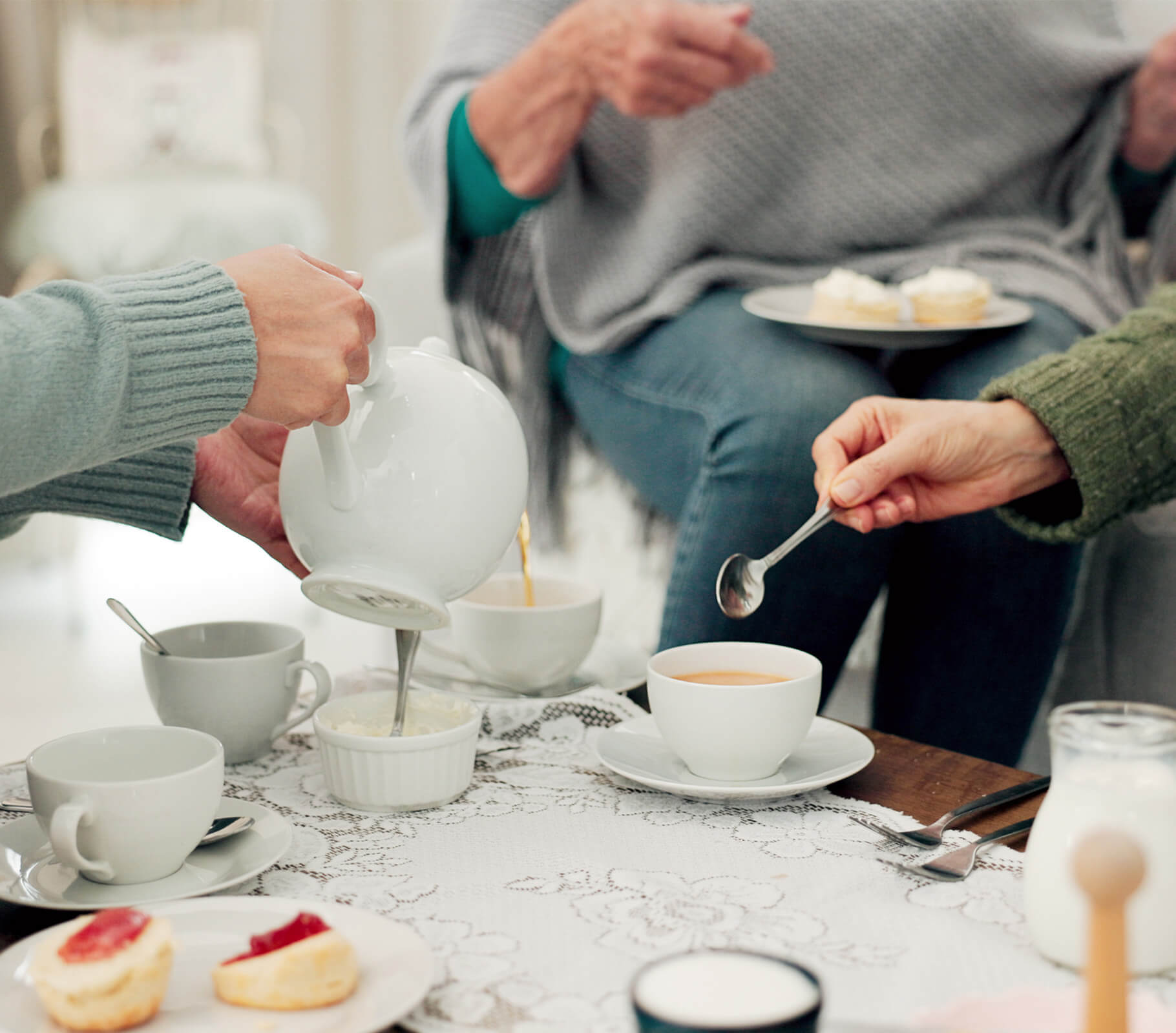 Residents in cozy attire enjoying a tea gathering with scones and tea on a lace-covered table.