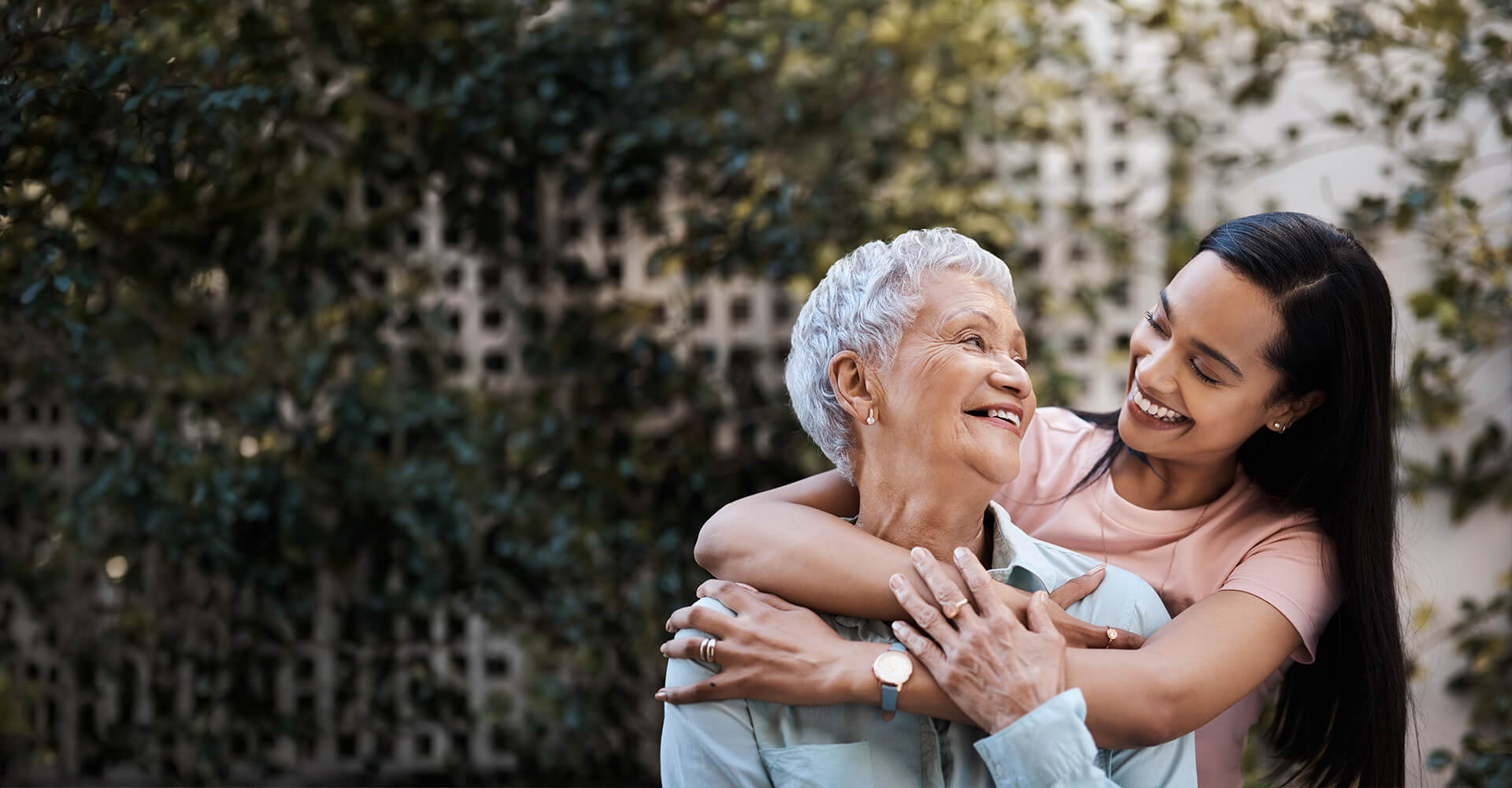 Elderly woman and young woman sharing a joyful embrace outdoors.