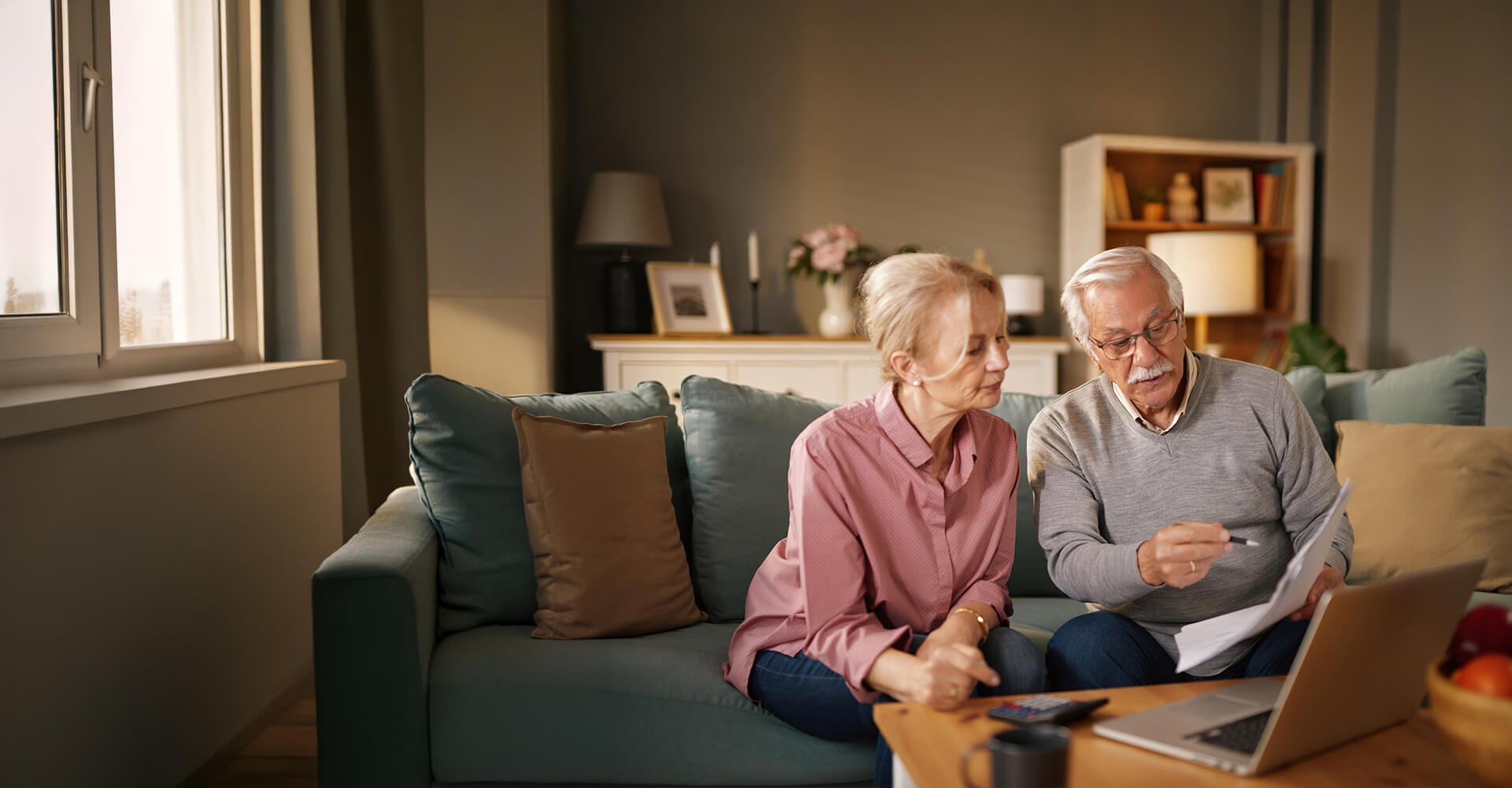 Elderly couple reviewing documents with laptop at home, discussing living community options.